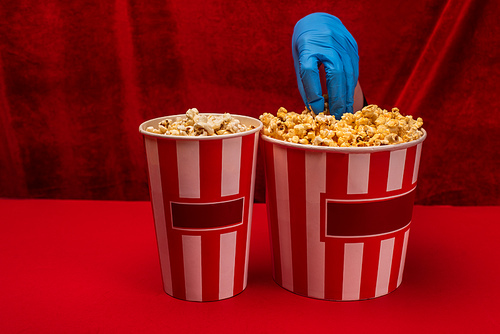 Cropped view of girl in latex glove holding popcorn on red surface and velour at background