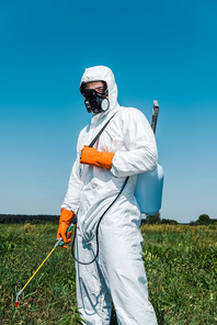 exterminator in white uniform and latex gloves holding spray against sky