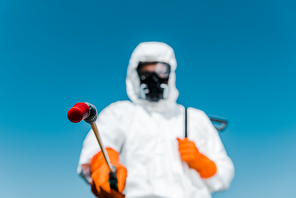 selective focus of exterminator in white uniform and latex gloves holding spray outside