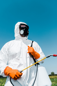 exterminator in orange latex gloves holding toxic spray against sky