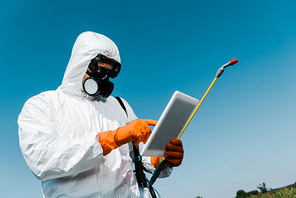 man in protective mask and uniform pointing with finger at digital tablet against sky