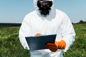 man in protective mask and uniform writing while holding clipboard