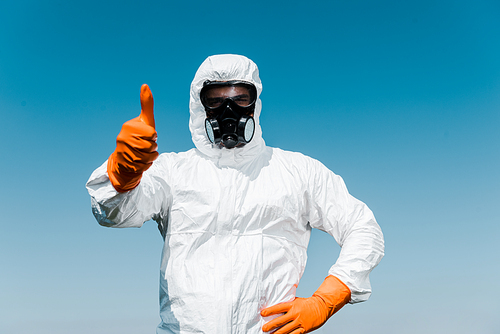 exterminator in protective mask and uniform standing with hand on hip and showing thumb up