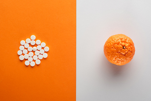 Top view of pills and mandarin on white and orange background