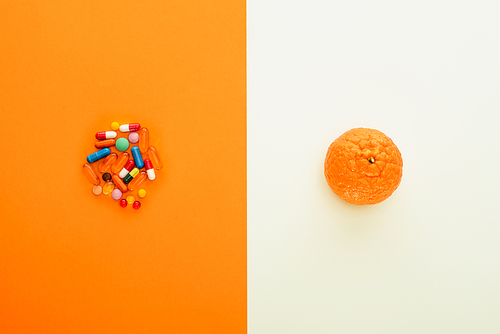 Top view of colorful pills and mandarin on white and orange background