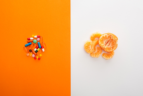 Top view of colorful medicines and mandarin on white and orange background