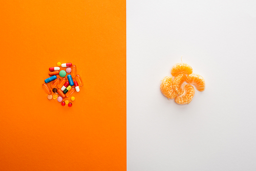 Top view of colorful pills and mandarin on white and orange