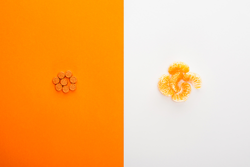 Top view of bright pills and mandarin on white and orange background