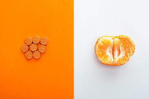 Top view of pills and mandarin half on white and orange background