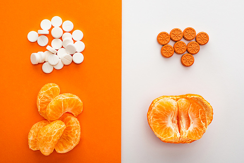 Top view of dietary supplements and mandarin on white and orange background