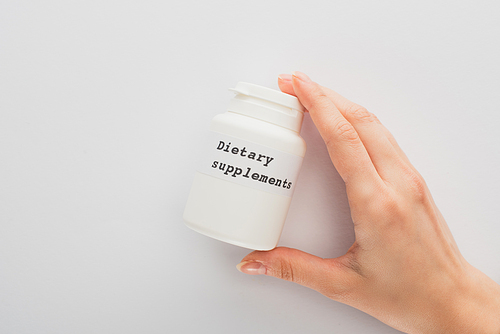 Cropped view of woman holding container with dietary supplements lettering on white background