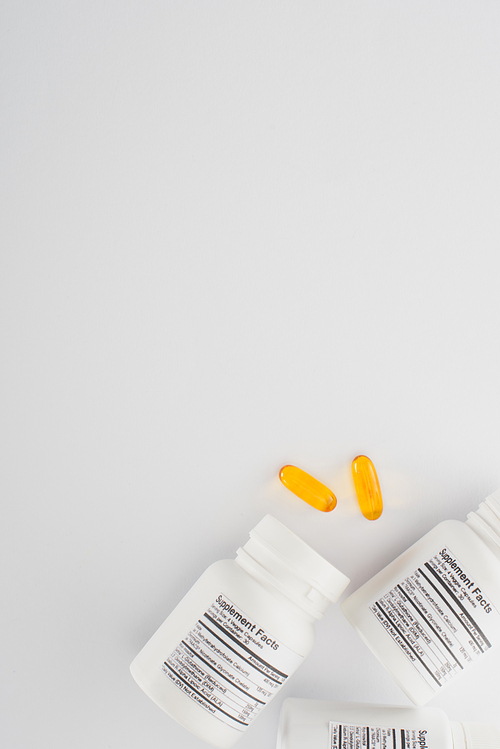 Top view of containers and fish oil capsules on white background