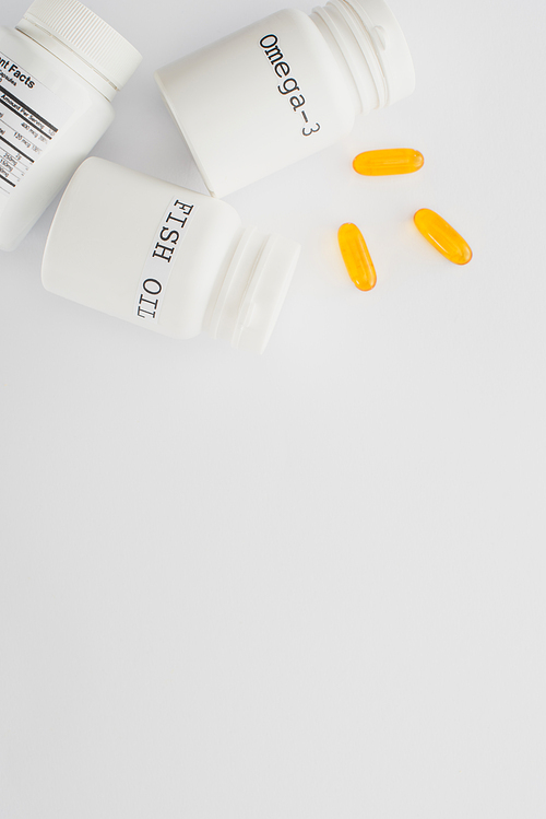 Top view of containers with fish oil and omega-3 lettering near yellow capsules on white background