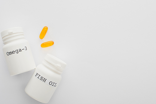 Top view of containers with fish oil and omega-3 lettering near capsules on white background