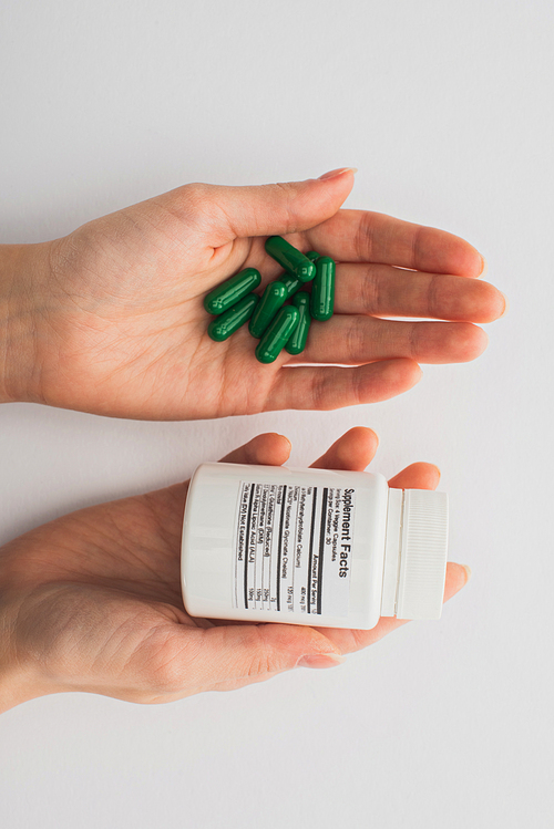 Cropped view of woman holding container and green capsules on white background