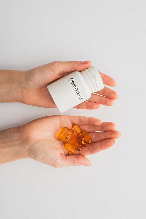 Cropped view of woman holding container with omega-3 lettering and capsules on white
