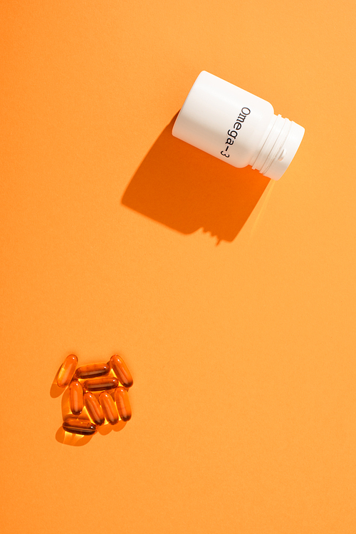 Top view of container with omega-3 lettering and capsules on orange background