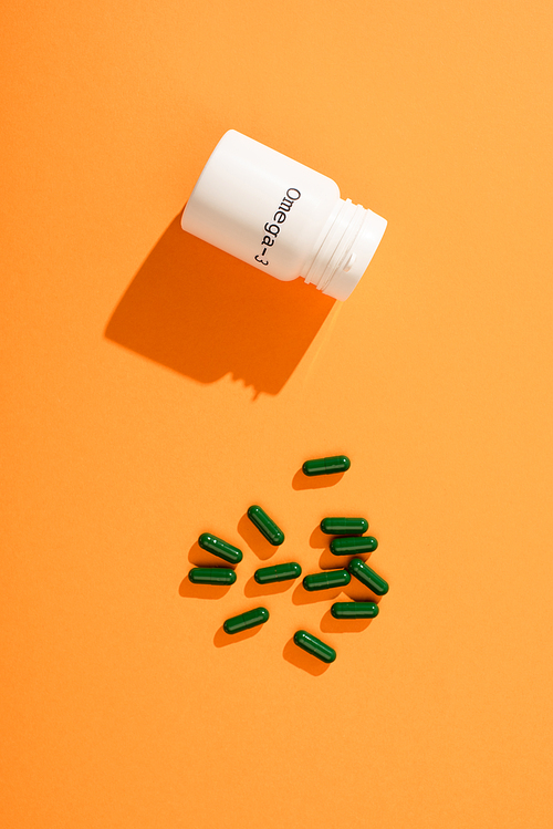 Top view of container with omega-3 lettering and green capsules on orange background