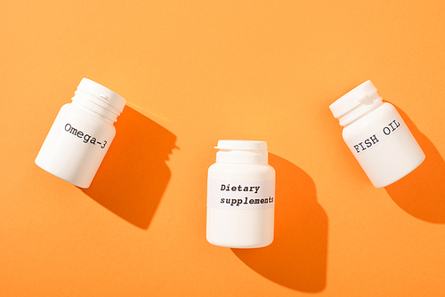 Top view of containers with omega-3, fish oil and dietary supplements lettering on orange background