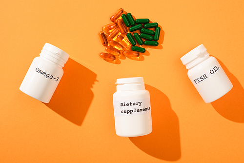 Top view of containers with omega-3, fish oil and dietary supplements lettering with capsules on orange