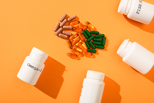 Top view of containers with omega-3 and fish oil lettering near capsules on orange background
