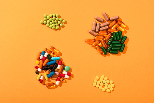 Top view of multicolored pills and capsules on orange background