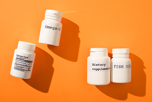 Top view of containers with omega-3, fish oil and dietary supplements lettering on orange background
