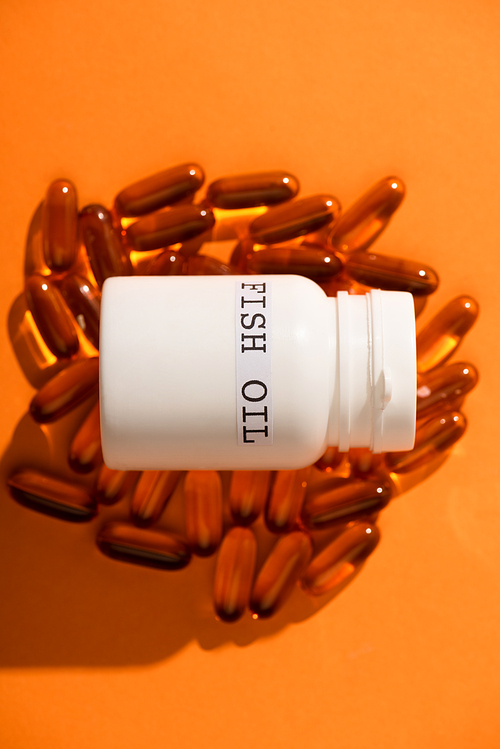 High angle view of container with fish oil lettering on capsules on orange background