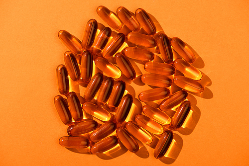 Top view of brown fish oil capsules on orange background
