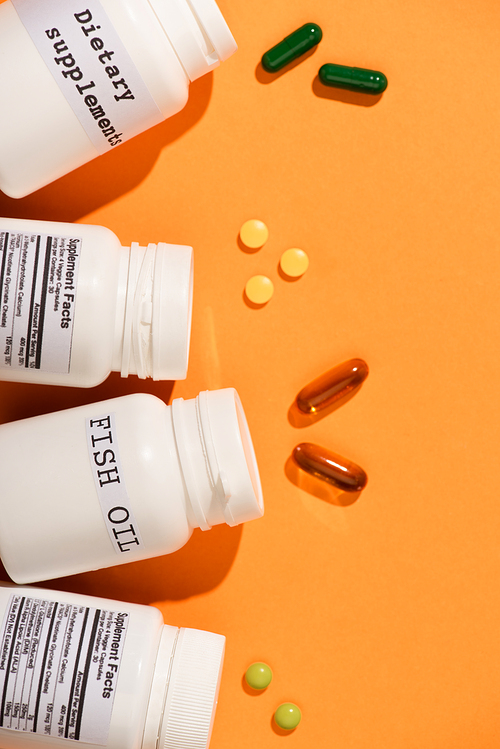 Top view of containers with fish oil and dietary supplements lettering near pills on orange background