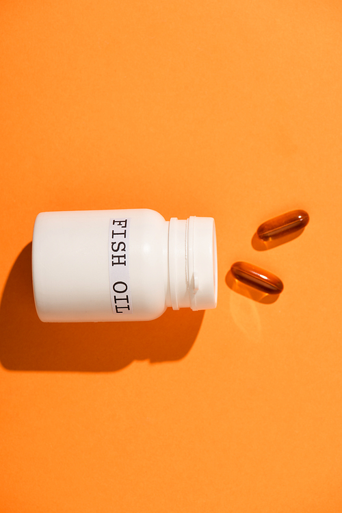 Top view of container with fish oil lettering near capsules on orange background