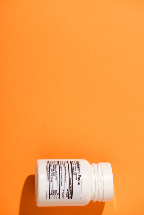 Top view of white container with dietary supplements on orange background