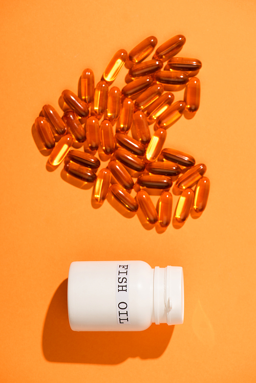 Top view of decorative heart from capsules and container with fish oil lettering on orange background