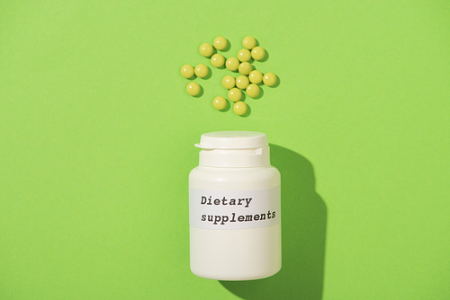 Top view of container with dietary supplements lettering and pills on green background