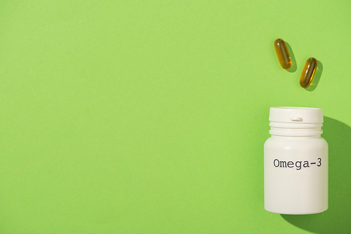 Top view of container with omega-3 lettering near capsules on green