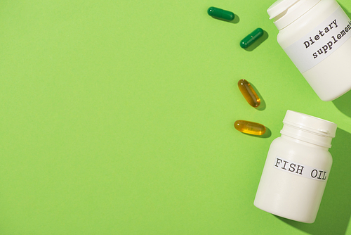 Top view of containers with fish oil and dietary supplements lettering with capsules on green