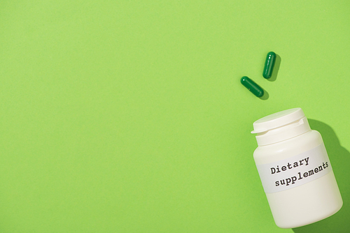 Top view of container with dietary supplements lettering and capsules on green