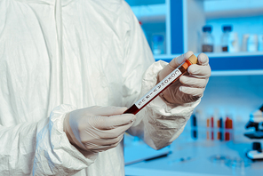 cropped view of scientist in latex gloves holding test tube with coronavirus lettering