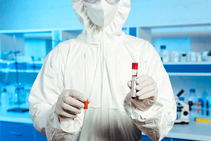 cropped view of scientist in latex gloves and medial mask holding test tube with coronavirus lettering