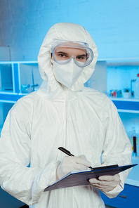 scientist in hazmat suit and goggles holding clipboard and pen
