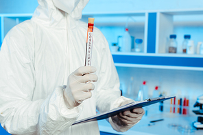 cropped view of scientist in hazmat suit holding test tube with coronavirus lettering