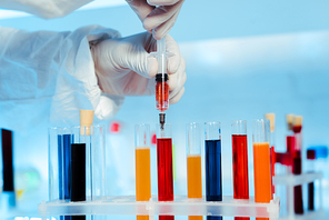 cropped view of scientist in latex gloves holding syringe near test tubes