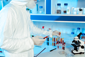 cropped view of scientist in latex gloves holding syringe and test tube with coronavirus lettering