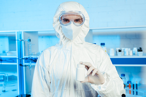 scientist in hazmat suit and goggles holding bottle in laboratory