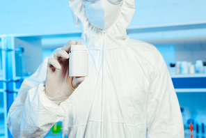 cropped view of scientist in hazmat suit holding bottle in laboratory