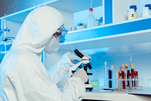 scientist in hazmat suit and goggles near microscope