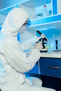 scientist in hazmat suit and goggles near microscope in laboratory