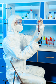 scientist in hazmat suit and latex gloves holding test tube with sample and coronavirus lettering