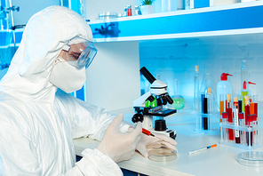 scientist in hazmat suit and goggles holding syringe near test plate