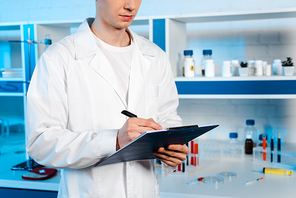 cropped view of scientist in white coat holding clipboard and pen in laboratory